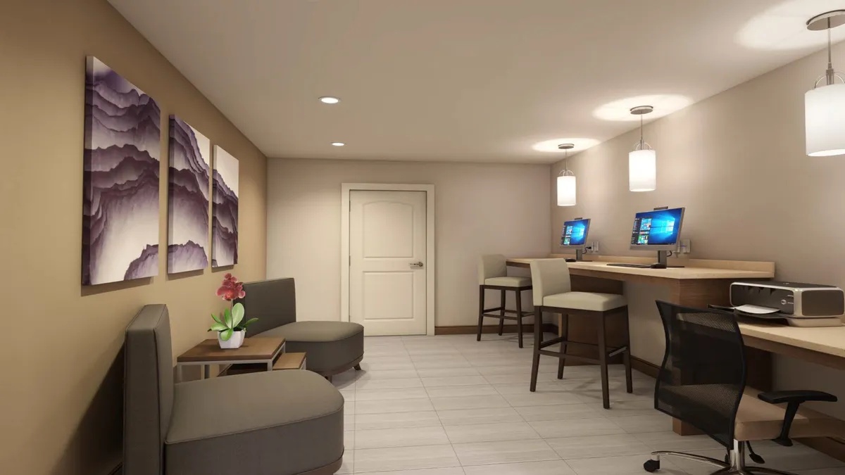 An interior scene featuring artwork on the wall, computer stations, and a comfortable seating area. The setup is well-lit and designed to accommodate both productivity and relaxation, with a modern, uncluttered style.