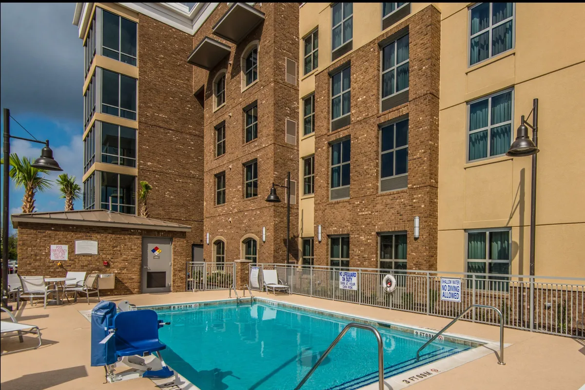 A serene view of the hotel’s outdoor swimming pool with ample lounge chairs, palm trees, and the building facade in the background. The pool area radiates a peaceful, sunlit mood ideal for both quiet mornings and lively gatherings.