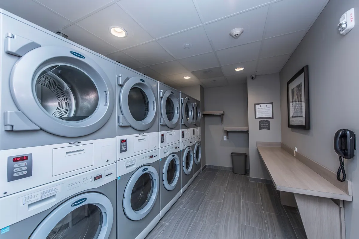This image shows a clean, organized laundry area with multiple washing machines and dryers, and a folding counter. The space is practical and tidy, emphasizing the convenience of self-serve laundry facilities for guests.
