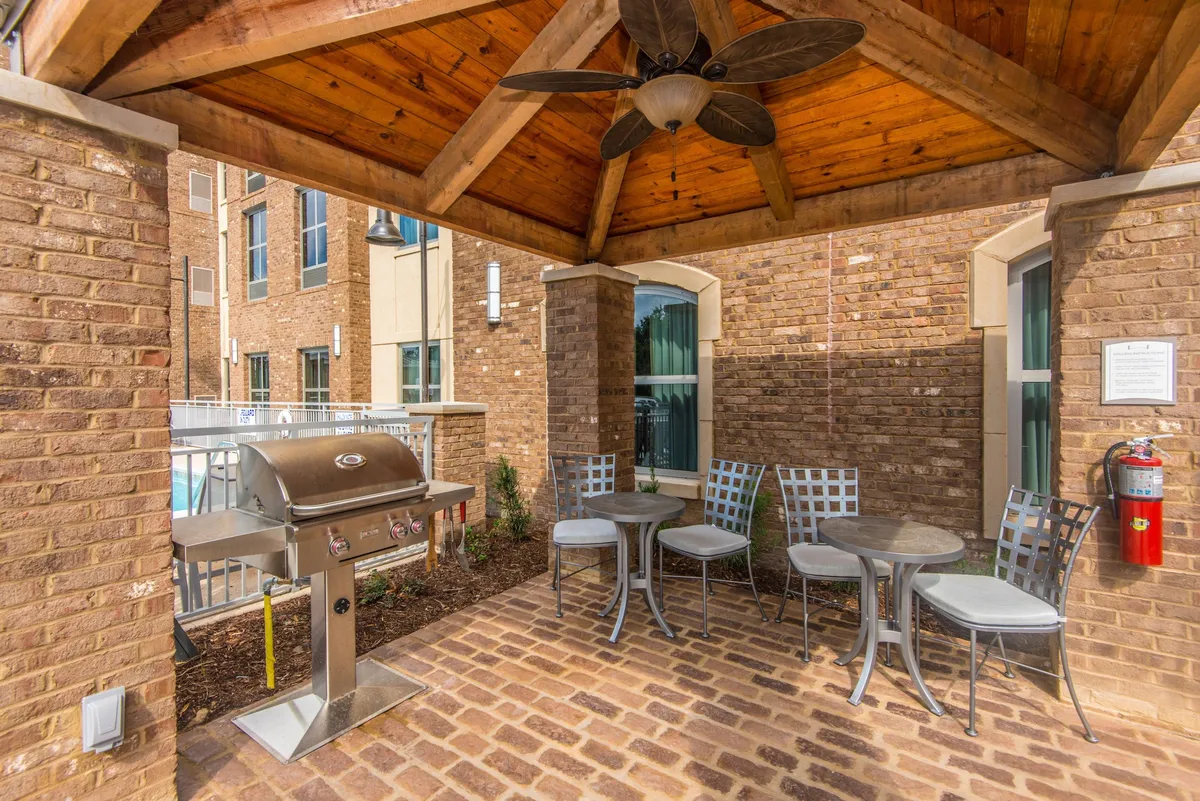 This exterior scene features a welcoming patio area equipped with a grill, ceiling fan, and comfortable seating. Guests are seen barbecuing, socializing, and relaxing outdoors in a casual, friendly atmosphere. The space is designed for gatherings, making it ideal for both informal meetings and winding down after a business day.