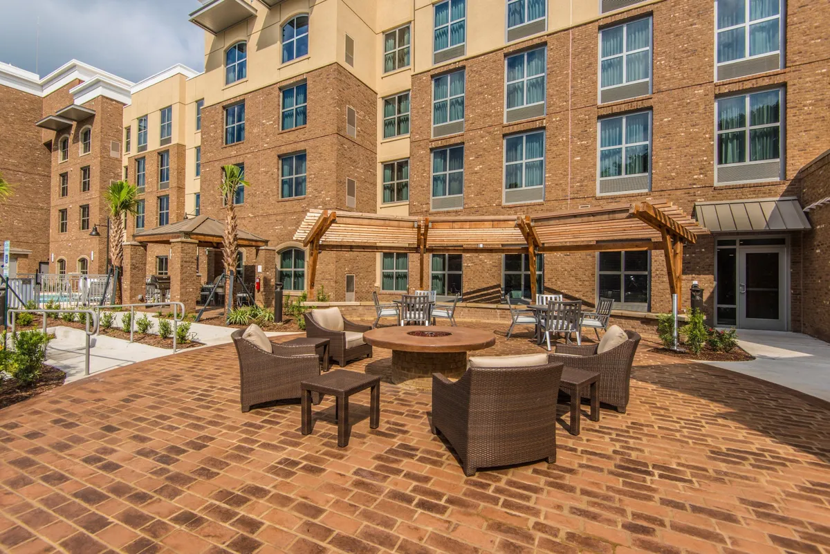 This exterior shot features a welcoming fire pit area with ample seating, palm trees, and the building’s facade in the background. The space feels lively yet intimate, perfect for evening gatherings or quiet coffee mornings.